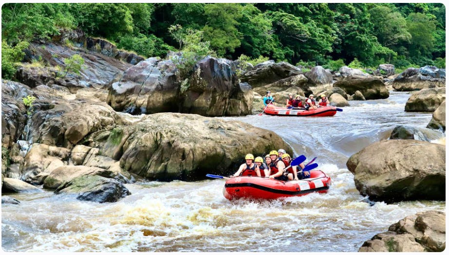 Tourists in a red raft navigating white water rapids on the Barron River, surrounded by the tropical rainforest near Cairns, Queensland.