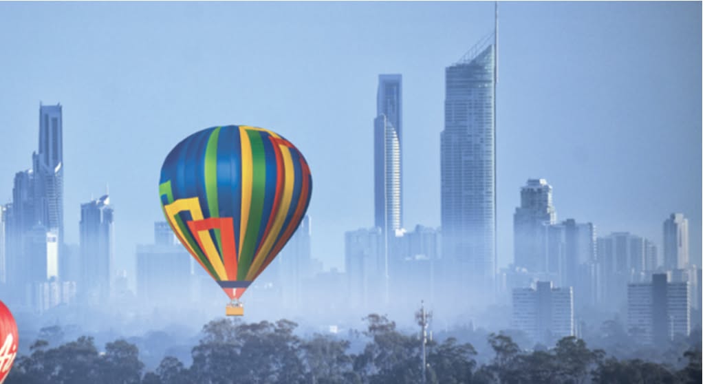 Colourful hot air balloon floating above misty trees near Gold Coast skyline Australia at sunrise