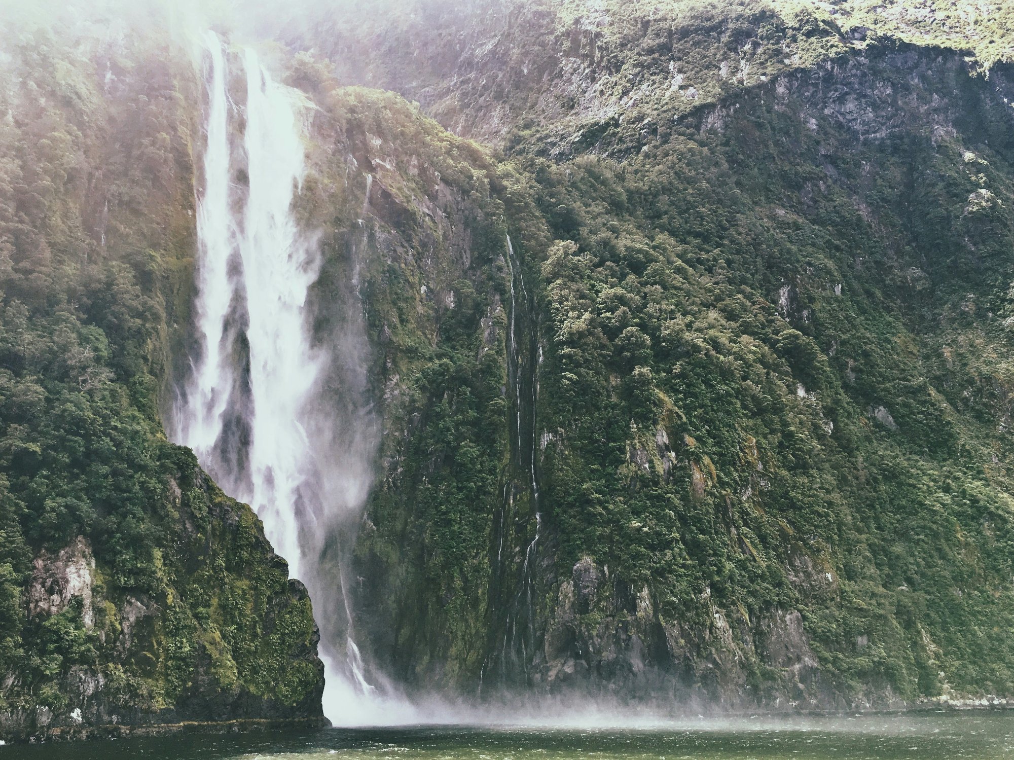 Stunning waterfall cascading down lush green cliffs in Milford Sound Fiordland New Zealand